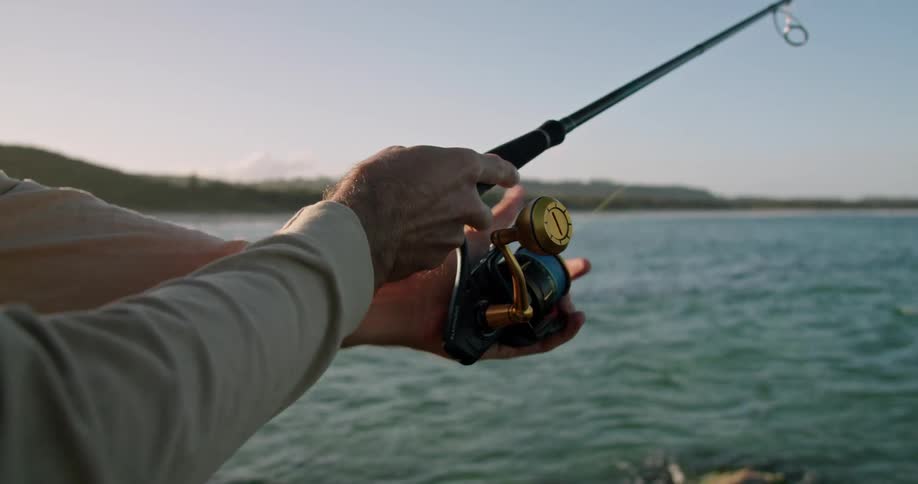 Close view of the hands of a man fishing from a rocky lake shore in the daytime