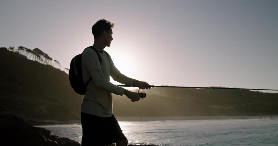 A man throws out a fishing line while fishing along the coast