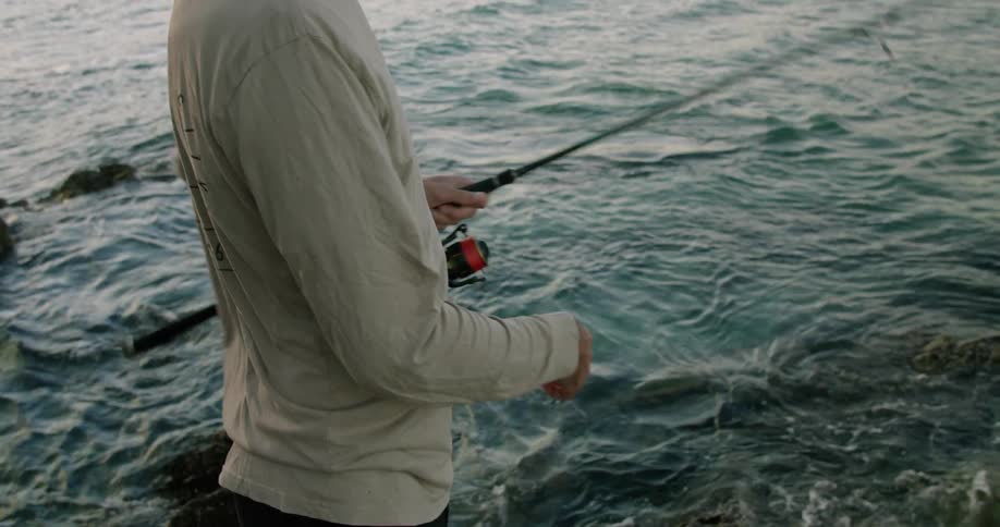 A man is fishing and he reels in his line to check the minnow on his fishing hook