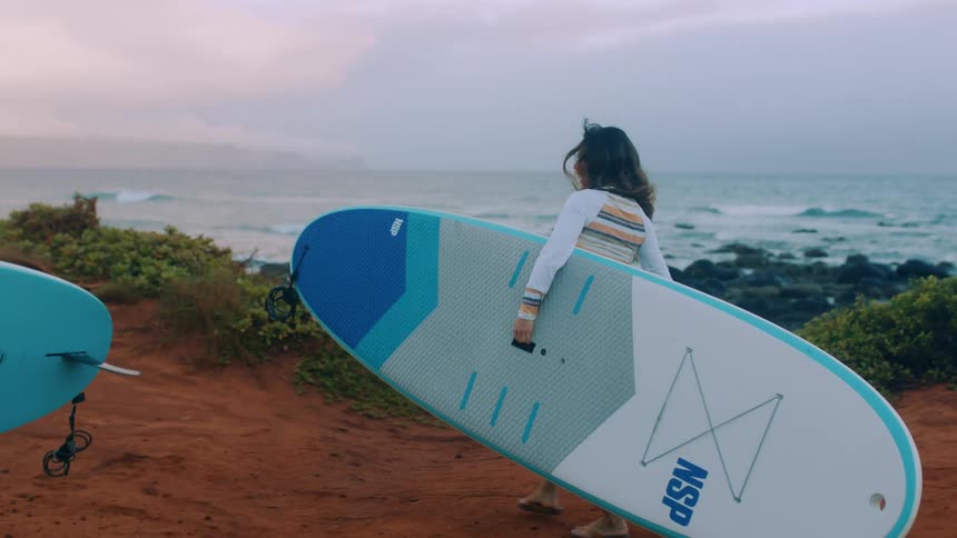 A man and woman carry their surfboards to the water