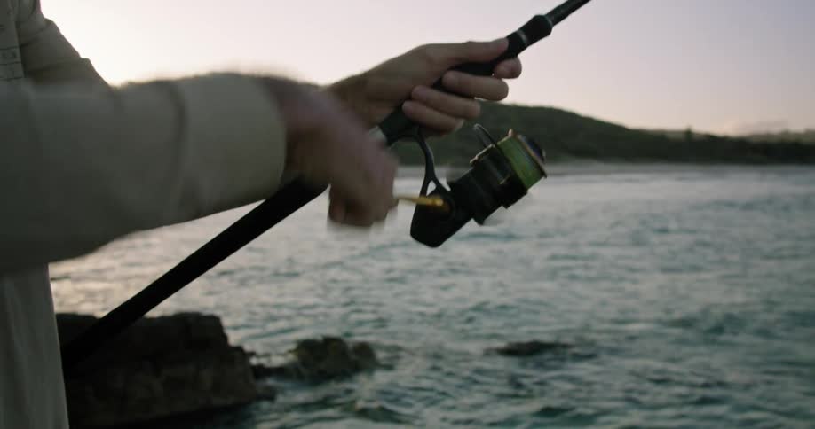 A man standing on the coast casts a fishing line before beginning to reel it in