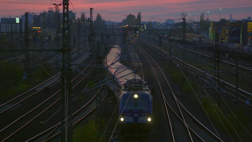 Train changes tracks with city skyline sitting under a red sky in background