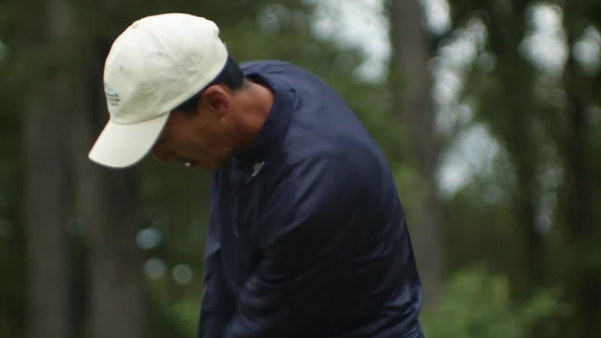Man with white cap and blue long sleeve shirt plays golf on golf course