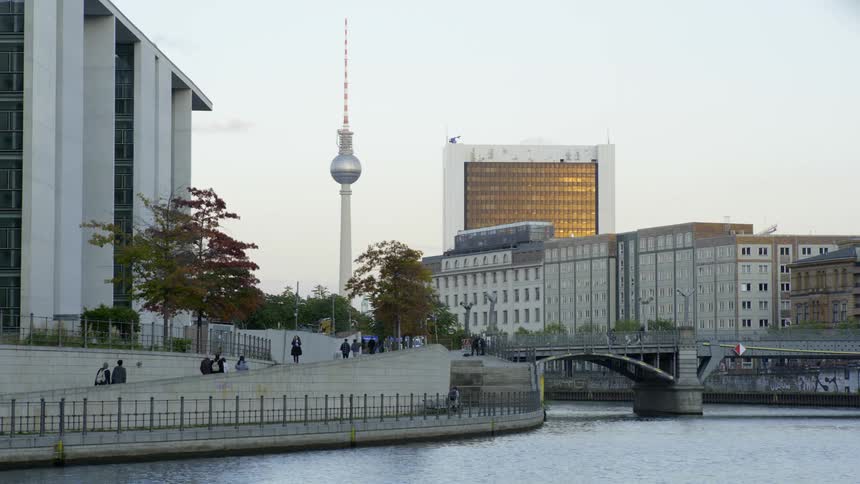 People walk past large office buildings along the river