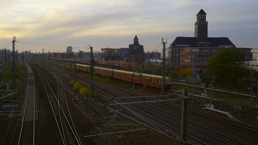 Passenger train moves along train tracks past buildings on overcast day
