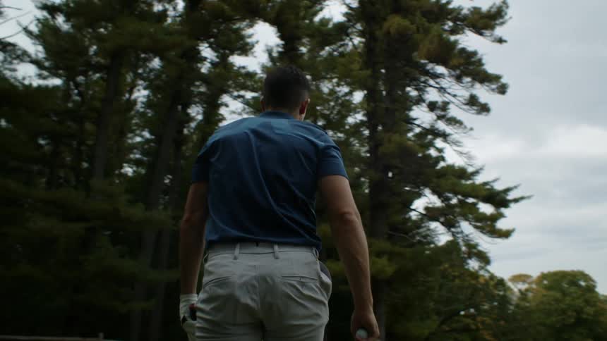 Man carrying a club and a golf ball walking on a golf course at morning