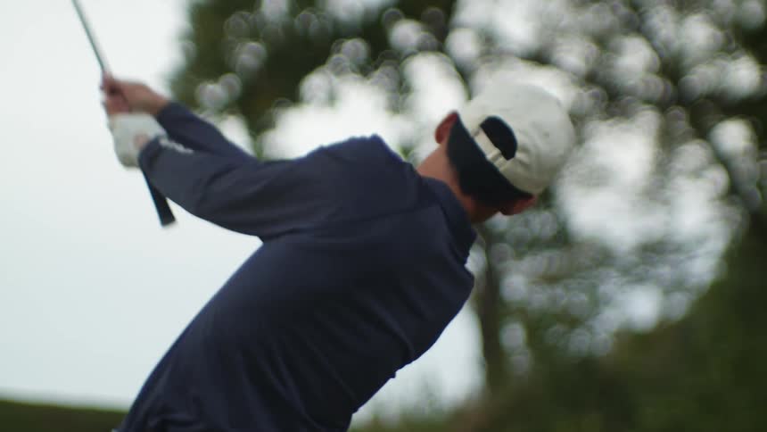 Golfer wearing white baseball cap takes swing with golf club
