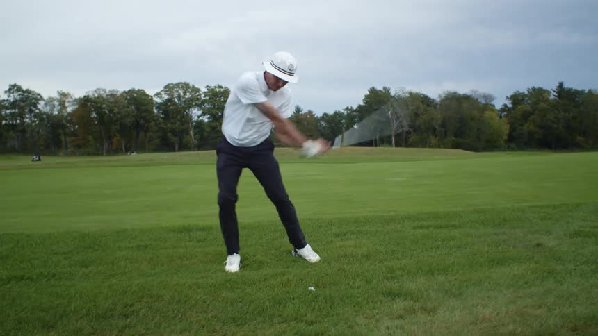 A man swings his golf club and hits a ball and watches where it goes