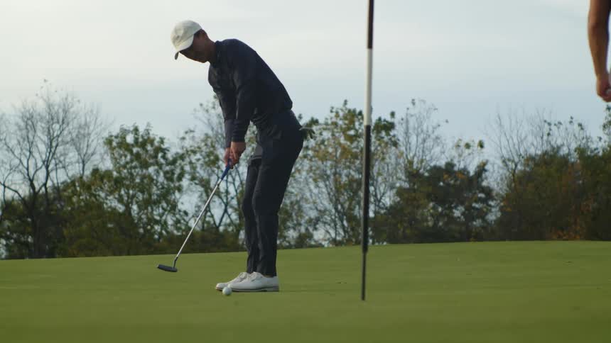 A man gently hits a golf ball towards a hole on a golf course during the day