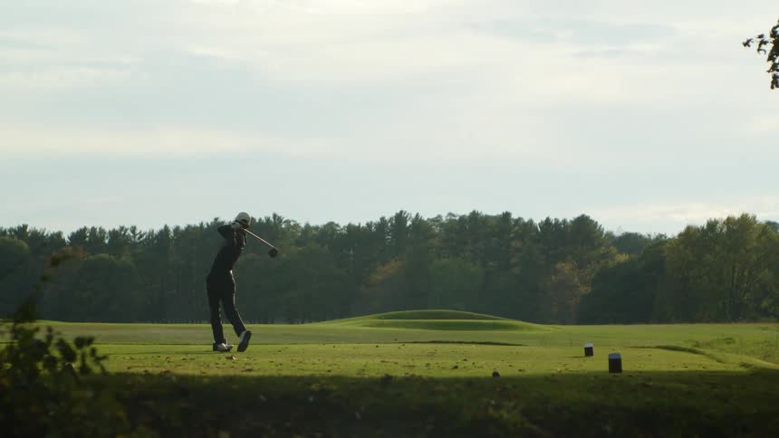 A man is hitting a golf ball with a club on a golf course during a windy day