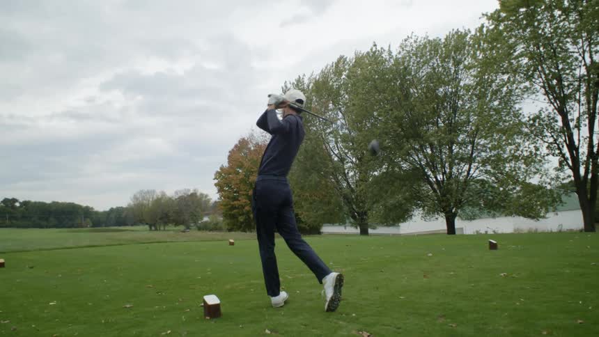 A man hits a golf ball at a driving range on a cloudy day