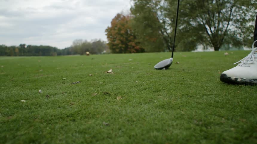 Golfer standing on course reaches down to pick up tee