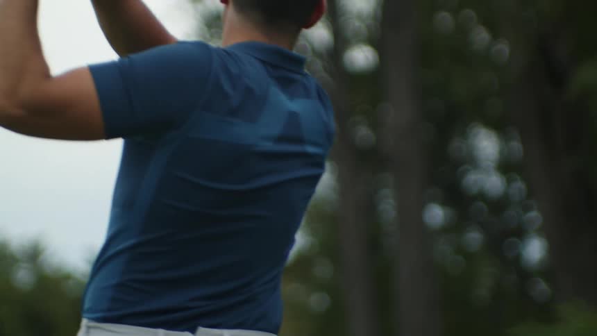 Man with blue polo shirt and brown pants plays golf on golf course