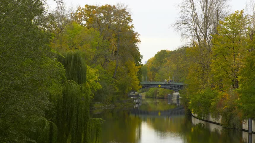 A pedestrian bridge over a river in a park on a cloudy day