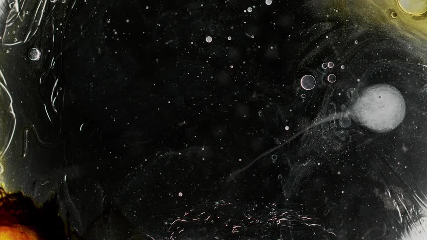 Reverse footage of ink blots flowing on water over a sheet of glass against a black background