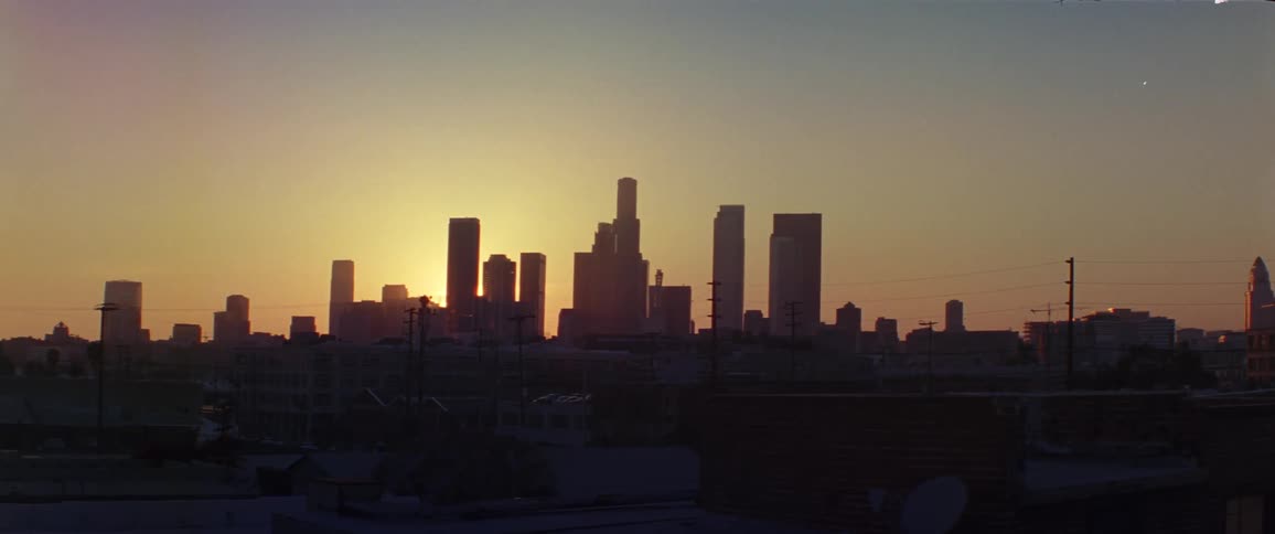 The sun is setting behind buildings and skyscrapers of a city skyline