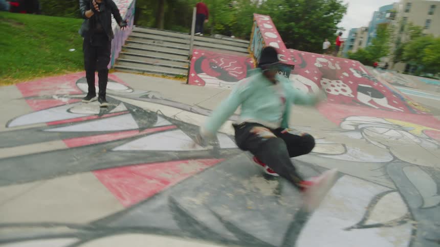 A man break dances in a skate park while being cheered on by a young woman on a cloudy day