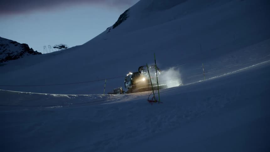 A snow plow is traveling down a ski slope at dusk