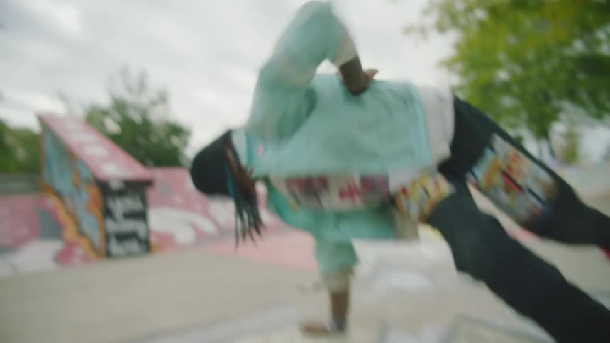 A teen break dances at a skate park holding a pose with legs in the air