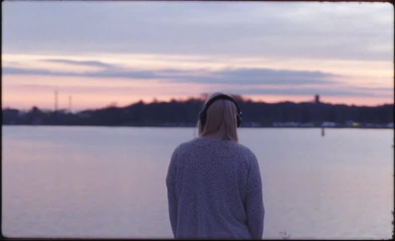 Blonde woman wearing headphones listens to music at the coast at dusk