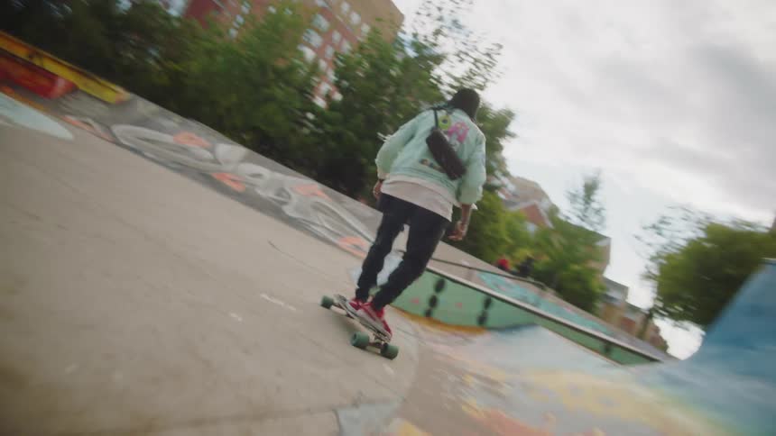 A man is riding a skateboard through a skateboard park and there are buildings in the distance