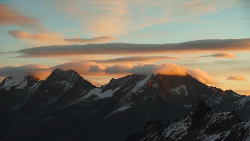 A view of a mountain range with snow during sunset