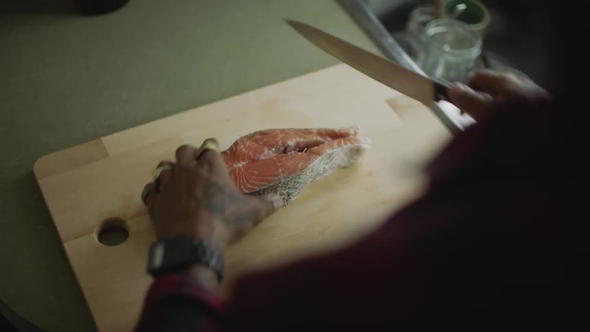 Person with tattoo hesitates before cutting fish steak sitting on chopping board