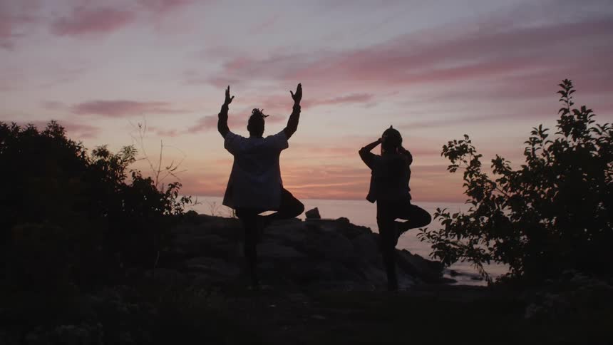 A man and woman meditate and do yoga while standing on a cliff over the ocean