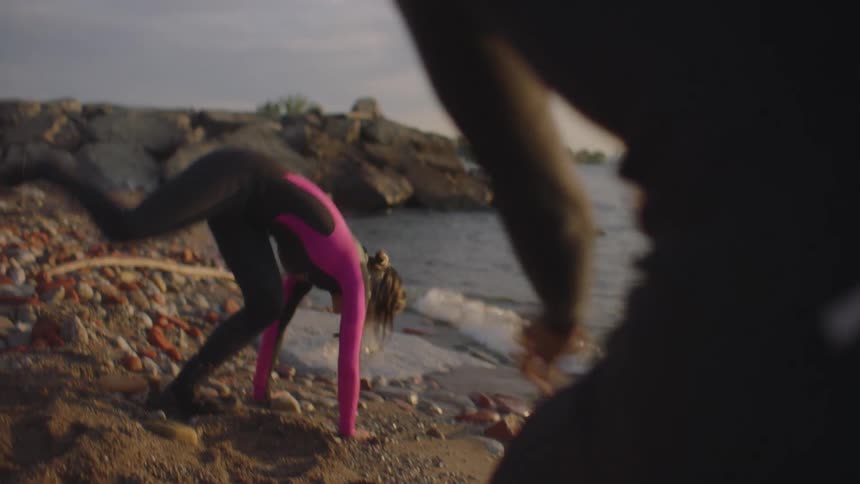 A woman does a cartwheel on the shore as she plays around with a man