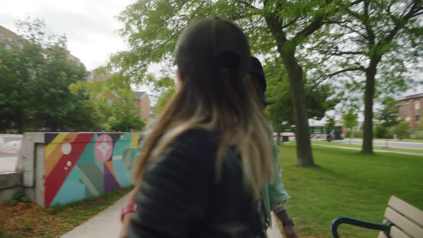 A girl walks up to a man doing a handstand on a park bench and greets him with an elaborate handshake