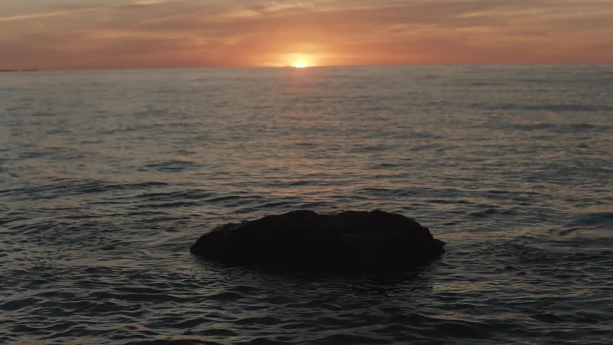 Sea rock is silhouetted against the sunset