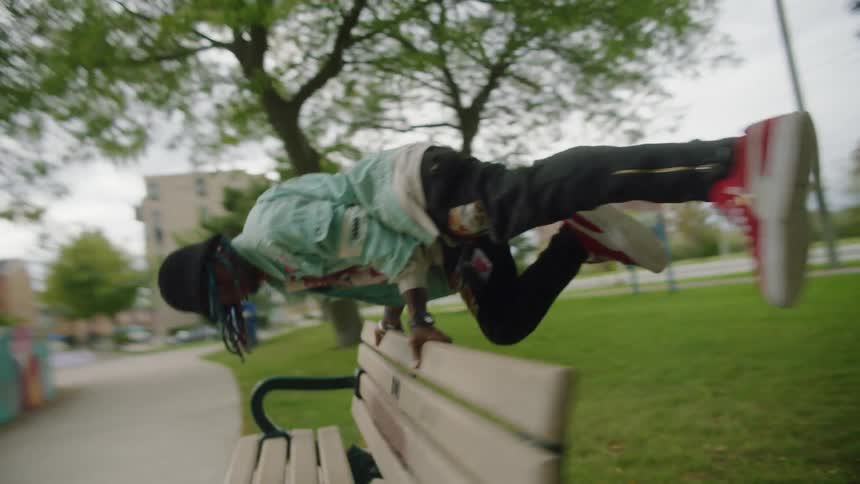 A man is balancing his body on the back of a bench in a public park on a cloudy day