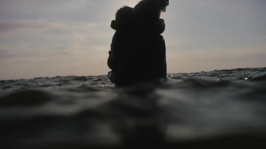A man and woman are standing in the ocean and embracing during the day