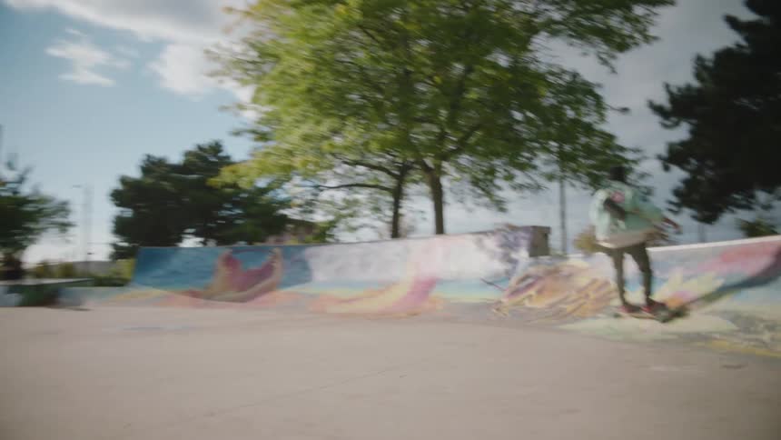 A man skateboards past a woman filming him with a smartphone in a skatepark during the day