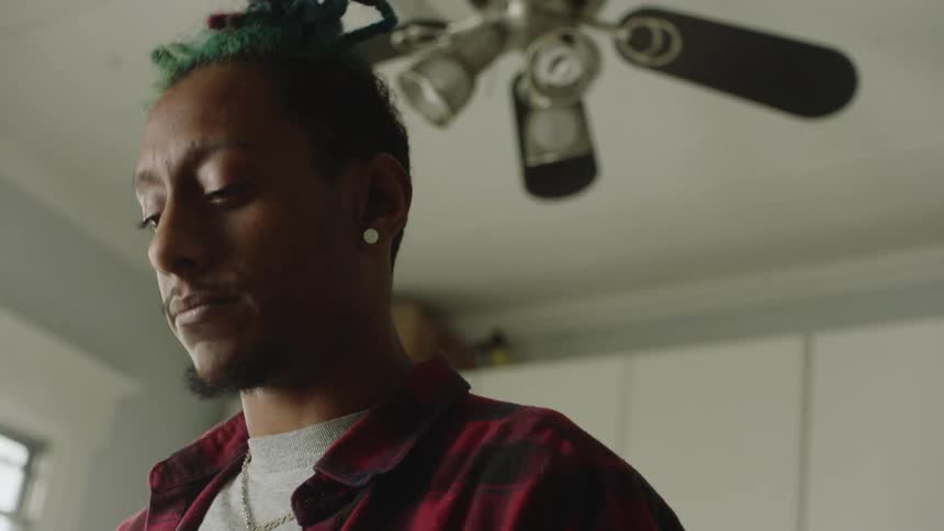 A man laughs and nods while standing under a ceiling fan in his kitchen