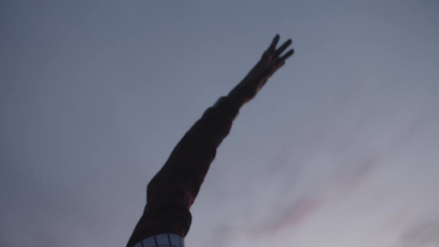 A man stretches his arm back while doing yoga along the coast