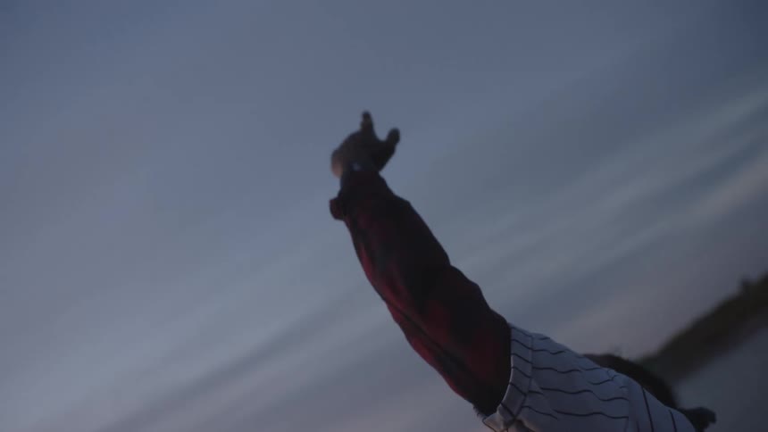 A man is standing on a beach with his arm and hand held up in the air