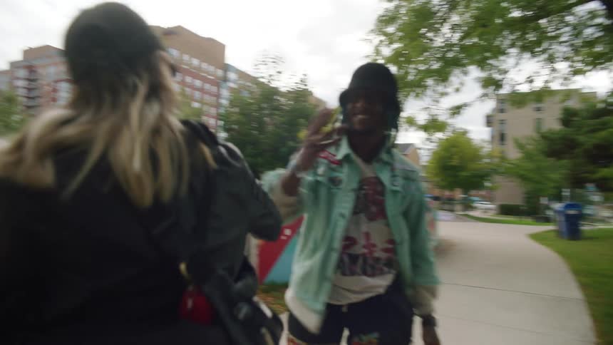 A woman greets a man break dancing off a bench in a skate park