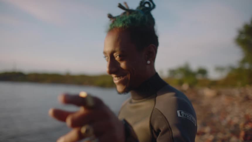 A man is standing on a beach smiling and moving his hands as he is talking to someone