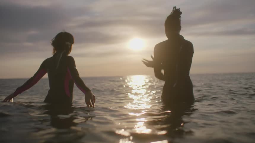 Woman and man standing in ocean let go of each others hand and reach up and out on sunny but cloudy day