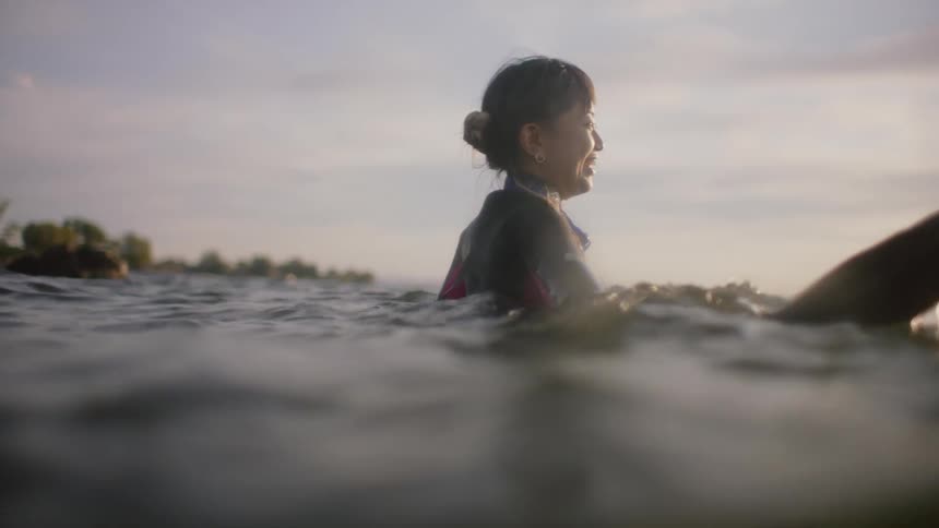 Couple wearing wetsuits walks in sea holding hands and smiling