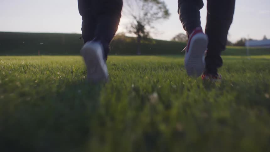 Two people are walking across a manicured grass field with hedges during the daytime