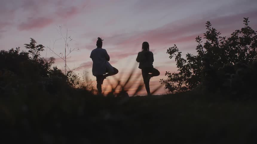 The silhouettes of two people doing a yoga pose outside