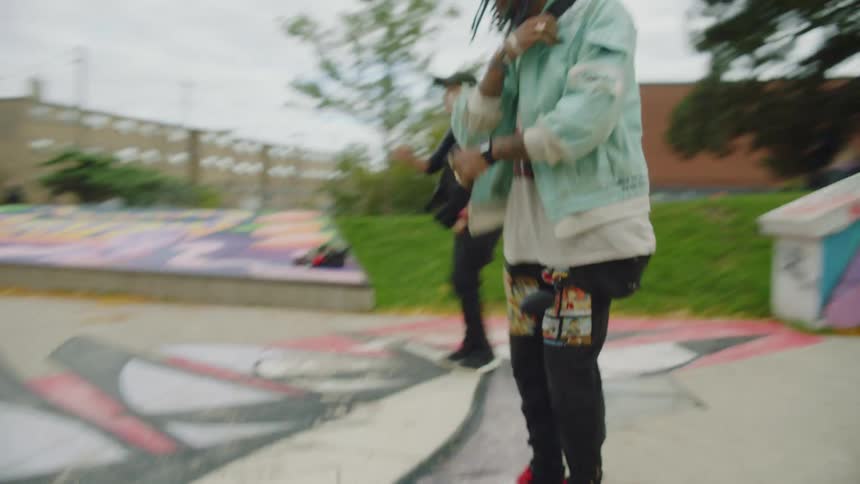 A young woman and man dance side by side in a skate park on a cloudy day