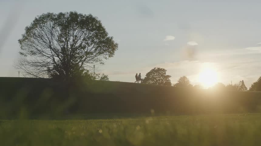 The silhouette of two people walking on a grassy ridge one carrying a golf bag