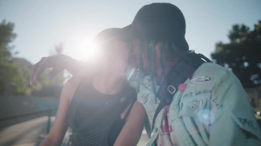 A young man sits outside with his arm around a woman and they laugh and rub noses together and kiss