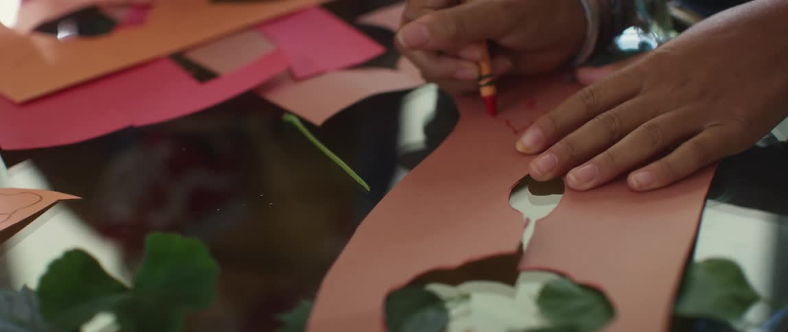 A person drawing over colored paper with crayon over a reflective surface