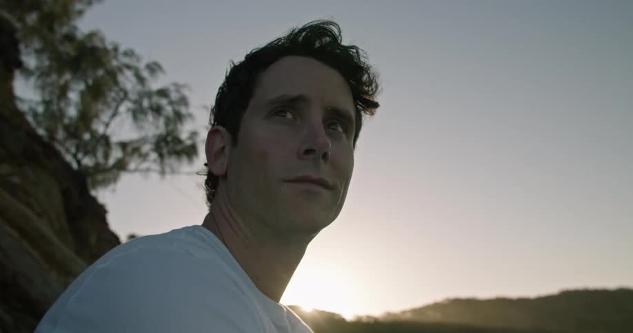 Man with white t shirt flies drone using remote control on the coast at sunset