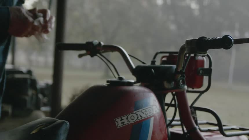 A man is standing next to an old honda motorcycle and turning the cap on the gas tank
