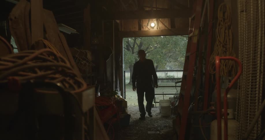 A man walks into a dimly lit barn used as storage